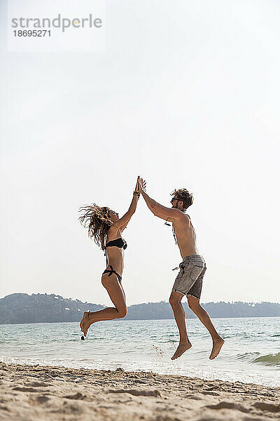 Glückliches Paar gibt High-Five-Springen am Strand