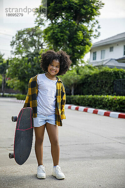 Smiling girl standing on footpath with skateboard