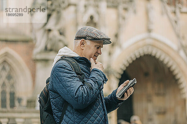 Älterer Mann benutzt Smartphone und steht vor der Kathedrale