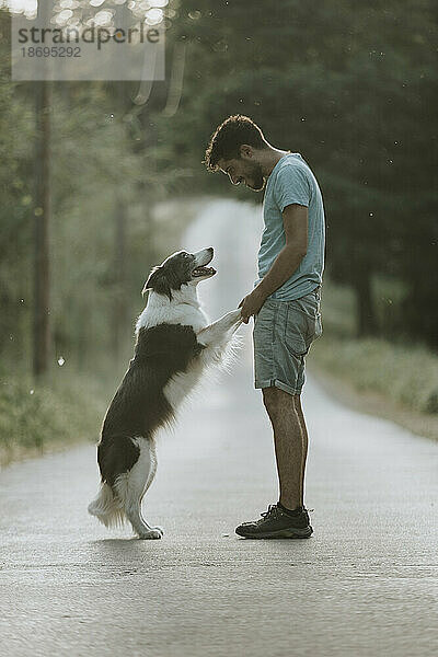 Young man standing with dog on road at sunset