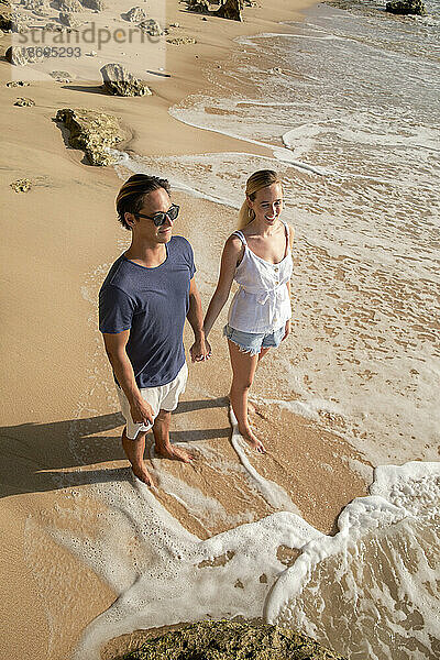 Happy young couple holding hands standing near shore at beach
