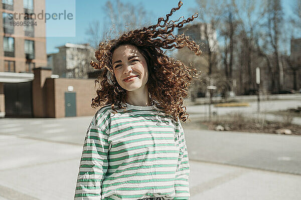 Lächelnde Frau mit zerzausten Haaren an einem sonnigen Tag