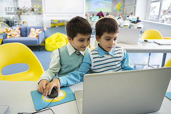 Jungen teilen sich Laptop und sitzen im Computerunterricht in der Schule