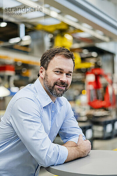 Lächelnder reifer Manager  der sich in der Industrie auf den Tisch lehnt