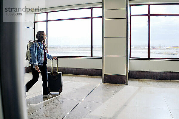 Junge Frau mit Koffer läuft in der Flughafenlobby