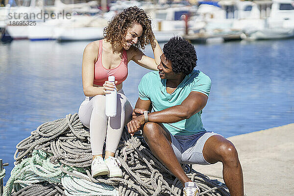 Mann zeigt Freundin  die am Seil am Hafen sitzt  Smartwatch