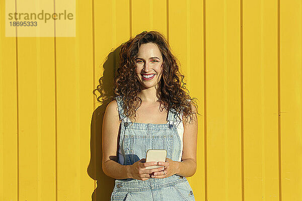 Glückliche Frau mit Smartphone vor gelber Wand