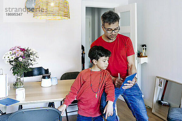 Son standing by father using tablet PC at home