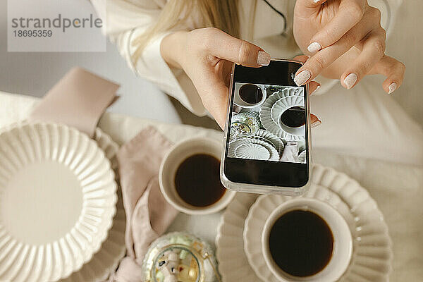 Frau fotografiert Kaffee zu Hause per Smartphone