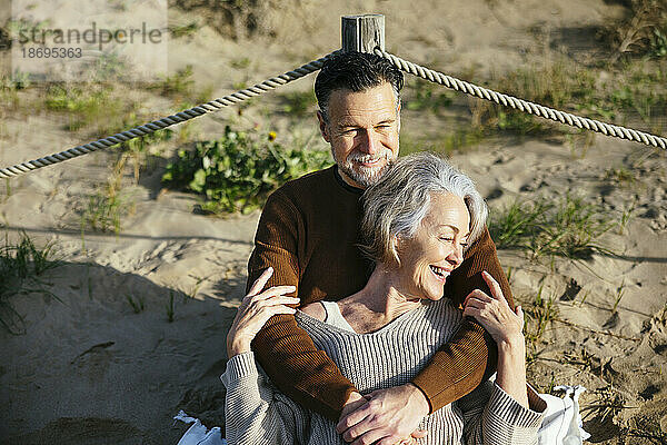 Smiling man embracing woman sitting at beach
