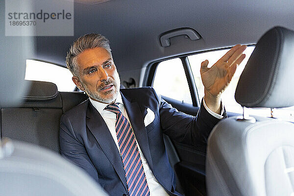 Reifer Geschäftsmann gestikuliert im Auto sitzend