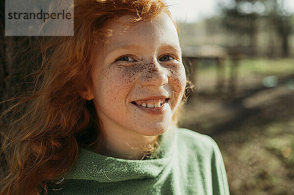 Lächelndes rothaariges Mädchen mit Sommersprossen an einem sonnigen Tag
