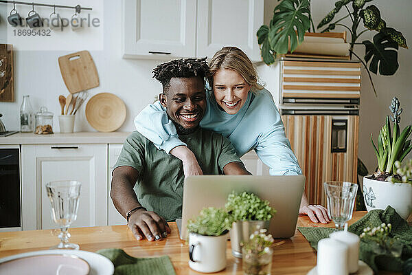 Lächelnde Frau schaut mit Mann zu Hause auf Laptop