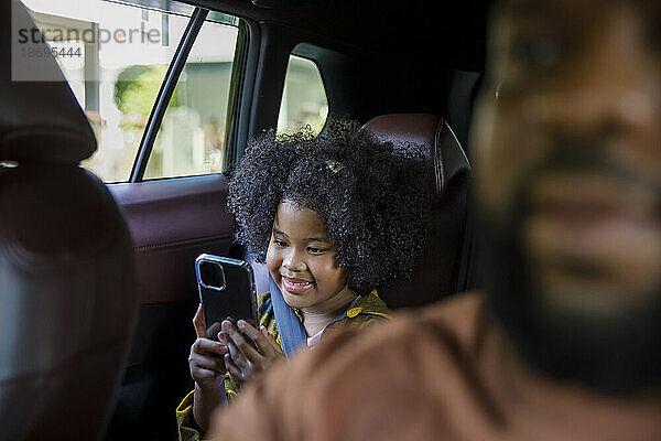 Lächelndes Mädchen  das im Auto ein Smartphone benutzt