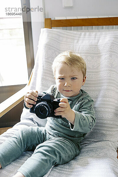 Baby Junge sitzt mit Kamera auf Stuhl zu Hause