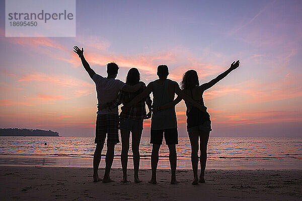 Silhouette unbeschwerter Freunde  die bei Sonnenuntergang am Strand stehen