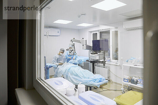 Arzt führt Augenoperation im Operationssaal durch  gesehen durch Glasfenster