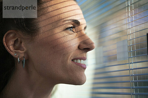 Lächelnde Geschäftsfrau mit Ohrringen  die im Büro aus dem Fenster schaut