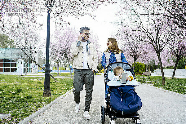 Vater und Mutter gehen mit Kinderwagen auf Fußweg im Park spazieren