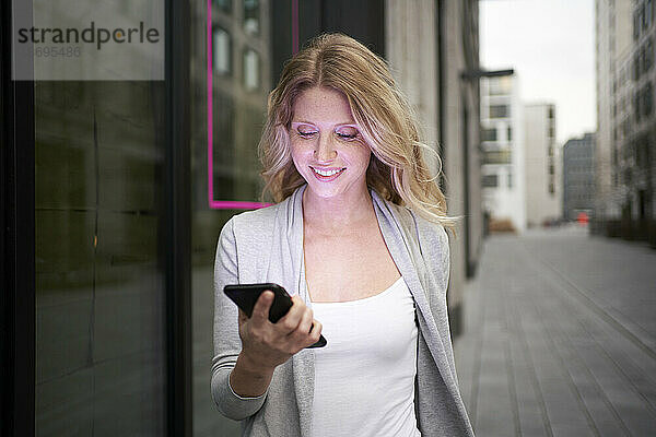 Lächelnde Frau hält Mobiltelefon am Bürgersteig