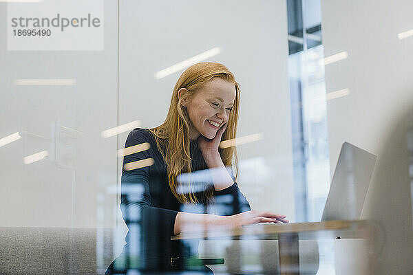 Lächelnde Geschäftsfrau  die am Laptop sitzt und in der Bürokabine sitzt
