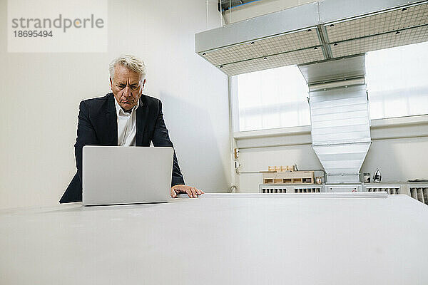 Leitender Geschäftsmann arbeitet am Laptop am Tisch in der Fabrik