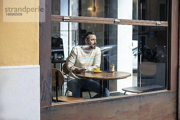 Nachdenklicher Mann sitzt im Café und sieht durch Glasfenster