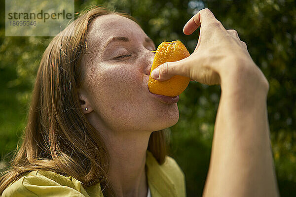 Frau mit geschlossenen Augen isst frische Orange im Obstgarten