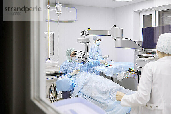 Augenarzt führt Augenoperation im Operationssaal durch  gesehen durch Glasfenster