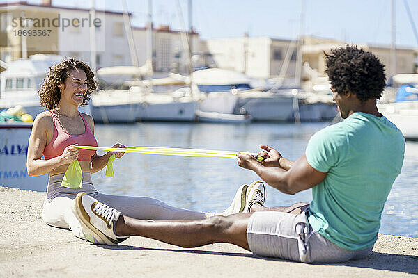Glückliches Paar trainiert mit Widerstandsband am Pier am Hafen