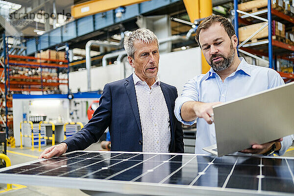 Manager hält Laptop und Geschäftsmann hält Solarpanel in der Fabrik