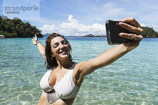 Sorglose Frau macht im Urlaub ein Selfie mit dem Smartphone im Meer