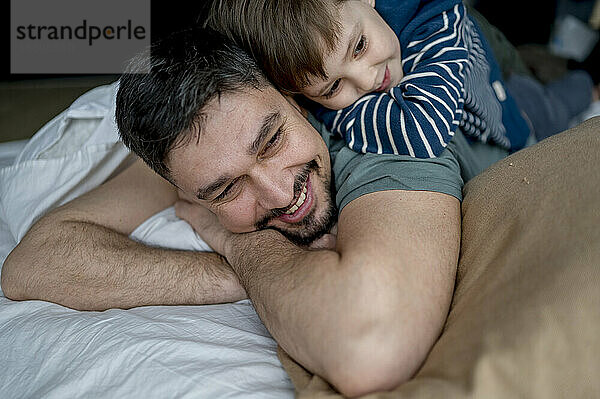 Glücklicher Mann  der mit seinem Sohn zu Hause im Bett liegt