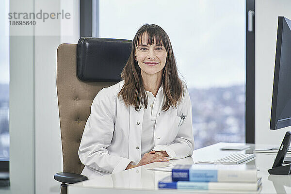 Porträt einer selbstbewussten Ärztin  die in der Arztpraxis am Schreibtisch sitzt