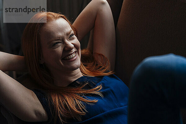 Cheerful woman with hands behind head lying on sofa