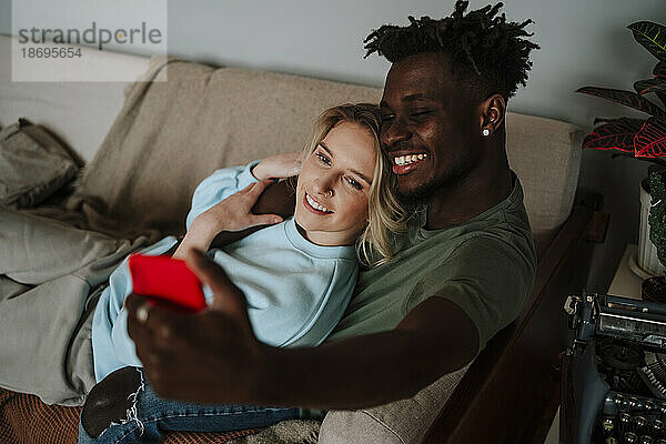 Lächelnder Mann macht ein Selfie mit seiner Freundin auf dem heimischen Sofa
