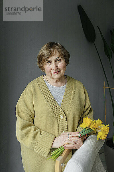 Ältere Frau steht mit Blumen in der Hand zu Hause