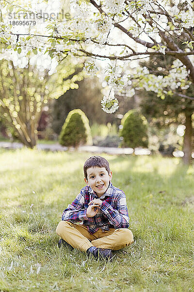 Smiling boy sitting cross-legged at back yard