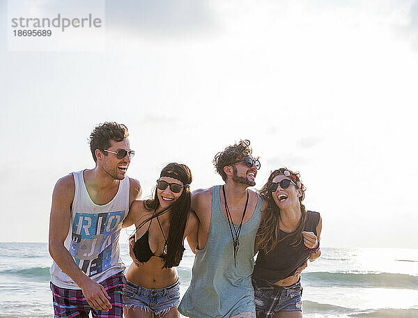 Fröhliche Freunde lachen mit den Armen am Strand