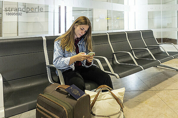 Junge Frau sitzt mit Smartphone auf einem Sitz in der Flughafenlobby