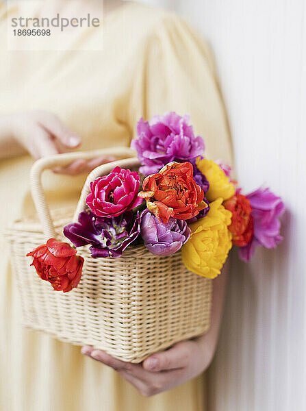 Frau hält Korb mit bunten Tulpen