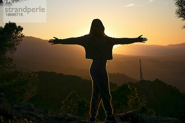 Silhouette of woman with arms outstretched at sunset