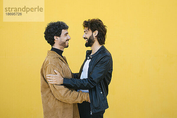 Happy gay couple standing against yellow background