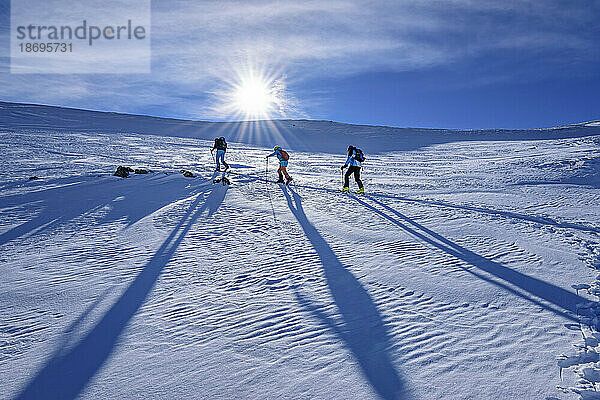 Österreich  Tirol  Die Sonne scheint über drei Skifahrern  die durch den Schnee in den Kitzbüheler Alpen fahren