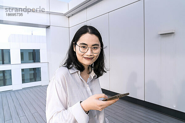 Porträt einer jungen Geschäftsfrau mit Mobiltelefon auf der Terrasse eines Bürogebäudes