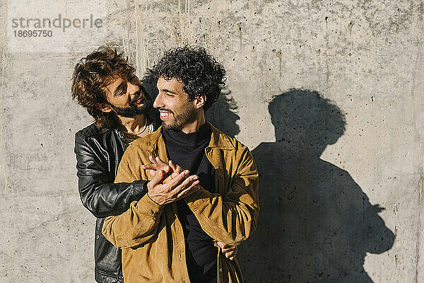Romantisches schwules Paar  das an einem sonnigen Tag vor einer Betonmauer steht