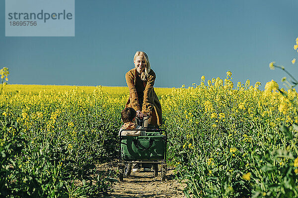 Mother pushing son in cart at rapeseed field