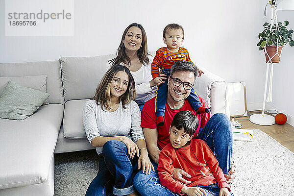 Lächelndes Mädchen sitzt mit glücklicher Familie im Wohnzimmer zu Hause
