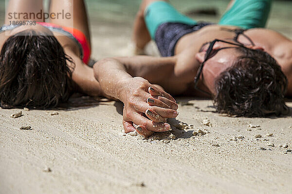 Couple holding hands lying on sand at beach
