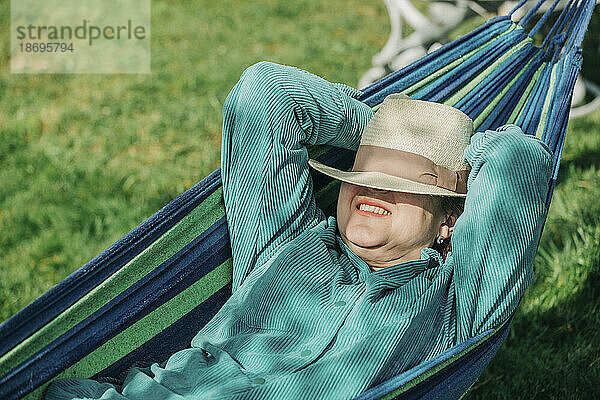 Ältere Frau mit den Händen hinter dem Kopf entspannt sich an einem sonnigen Tag in der Hängematte